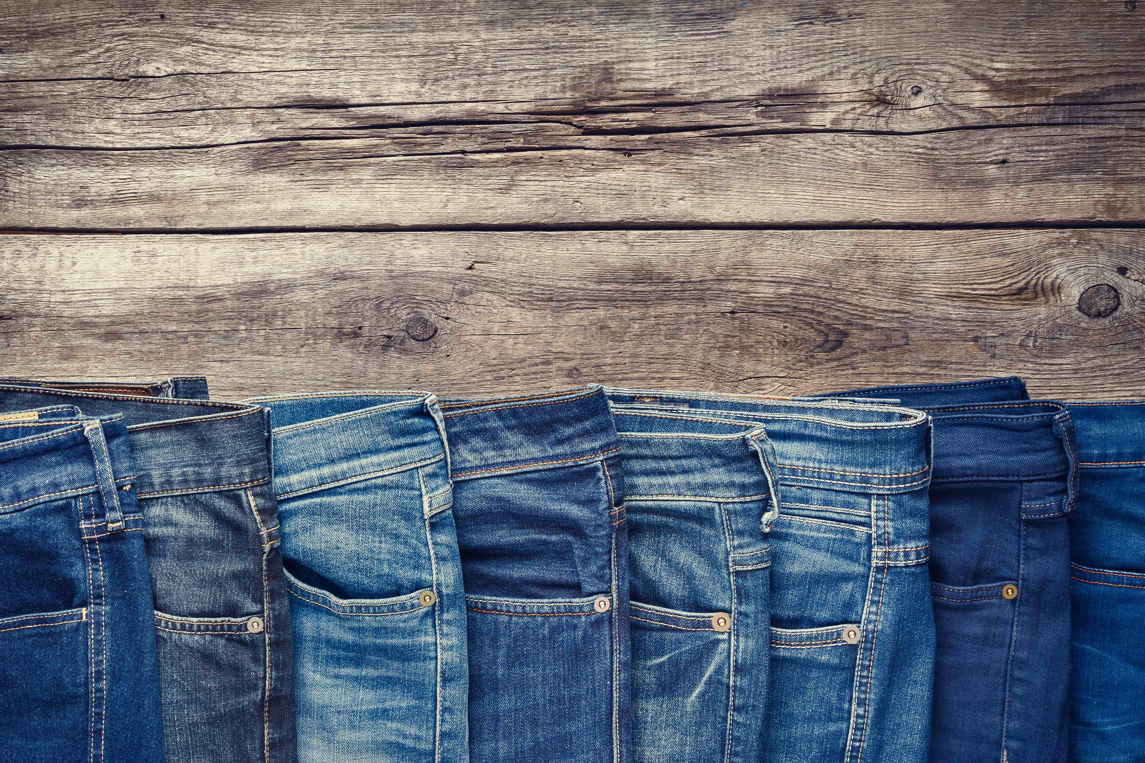 Many different denim jeans on wooden table.jpg